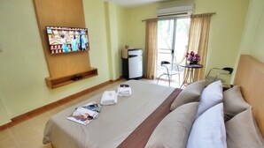 A hotel room with a bed, a television mounted on the wall, a small table with a chair, and a refrigerator. - Suklutai Hotel & Serviced Apartment (Bang Khla)