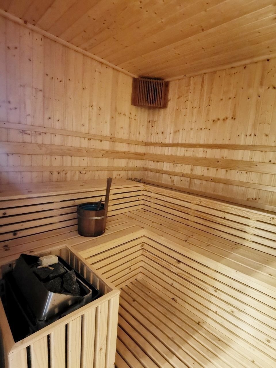 A sauna room with wooden walls and benches, a bucket, and a heater.