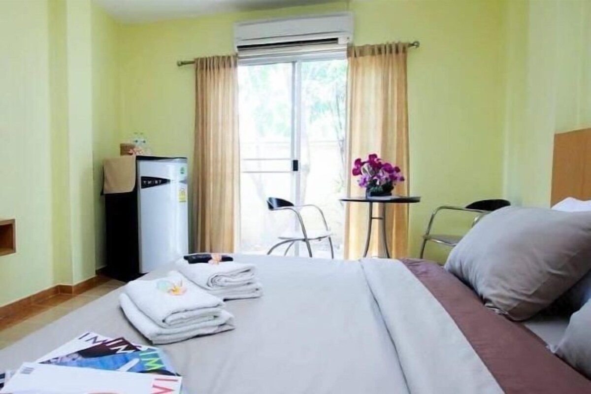 Ein Hotelzimmer mit einem Bett, einem Schreibtisch, einem Sessel, einem Kühlschrank und einem Vorhangfenster.