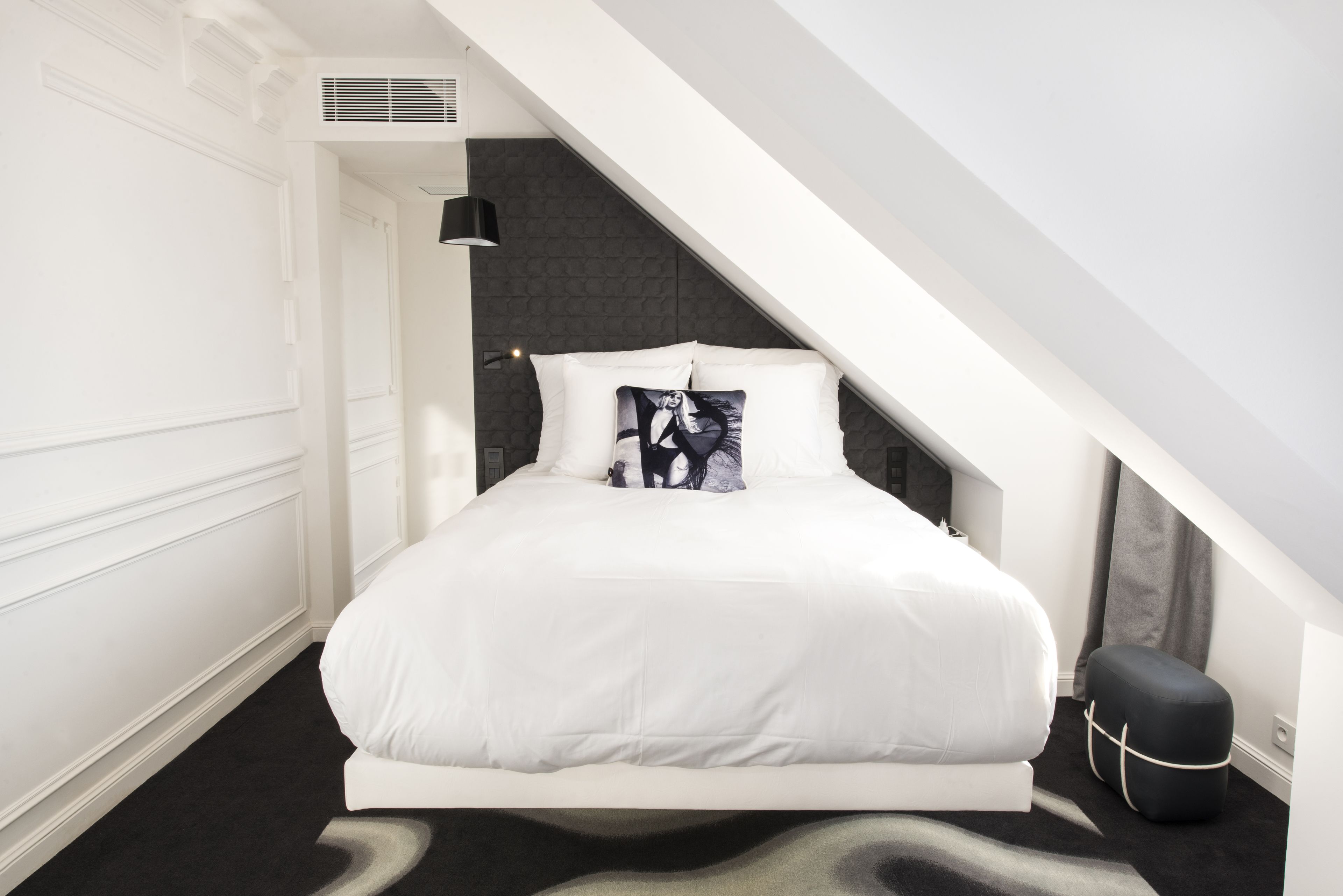 Une chambre à coucher moderne avec un lit blanc, une tête de lit noire et un pouf noir.