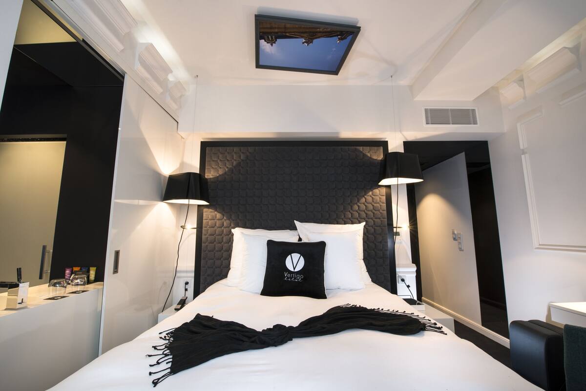 A modern hotel room with a large bed, a skylight, and a black headboard.
