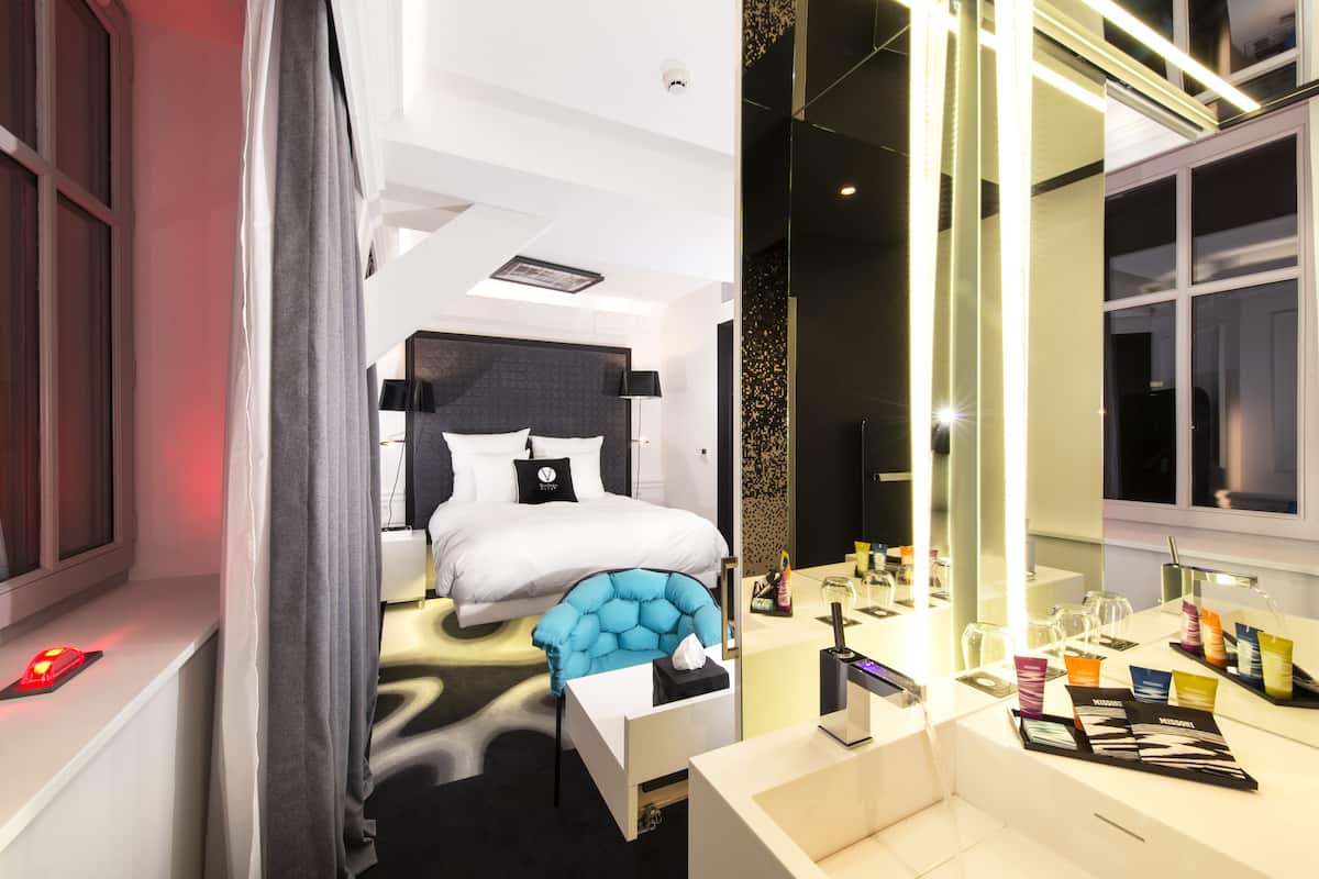 A modern hotel room with a large bed, a vanity with toiletries, and a window with curtains.