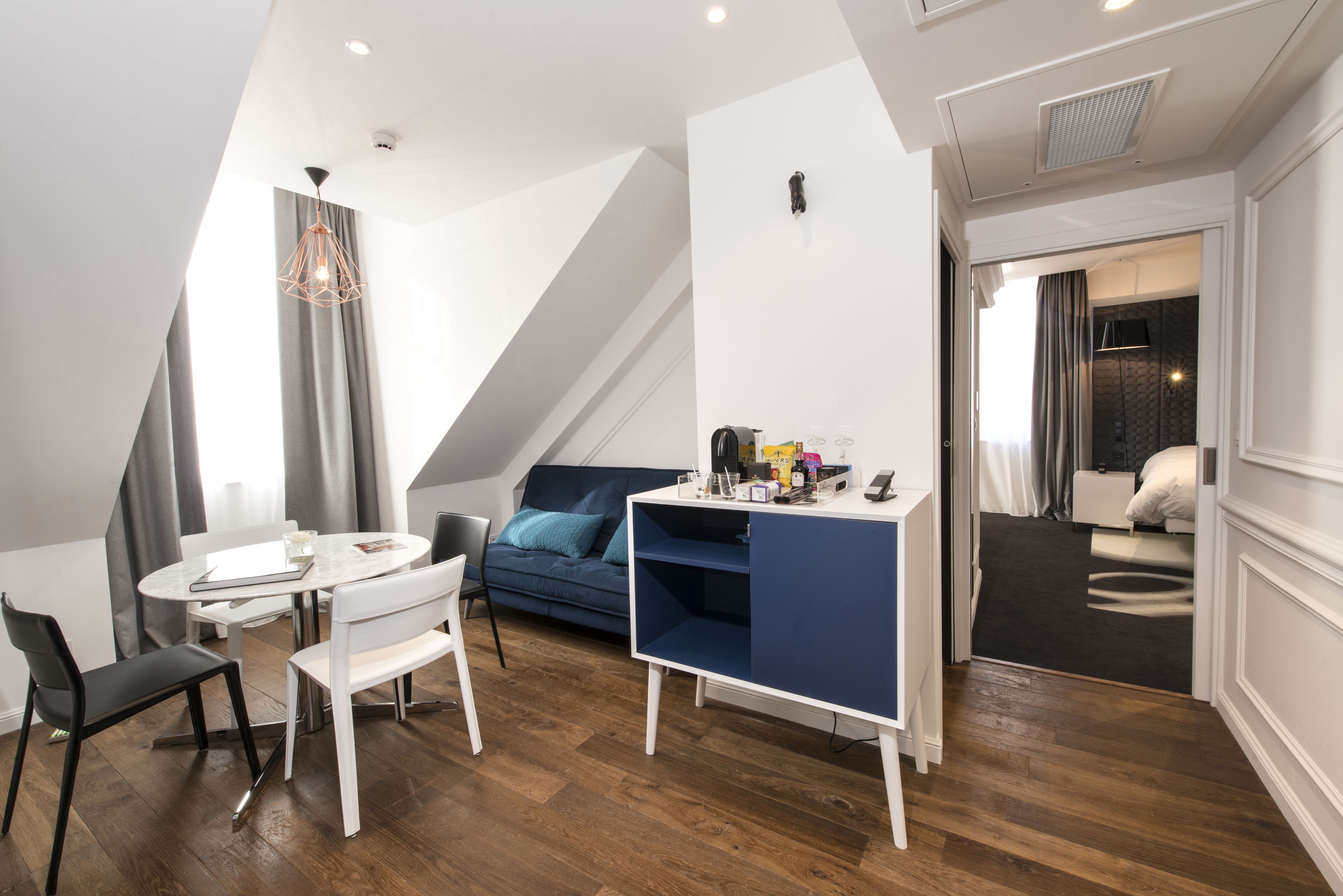 A modern room with a white desk, a blue sofa, and a dining table with chairs.