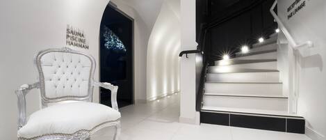 A white, tufted chair in a modern, well-lit hallway with a staircase leading to an upper level.