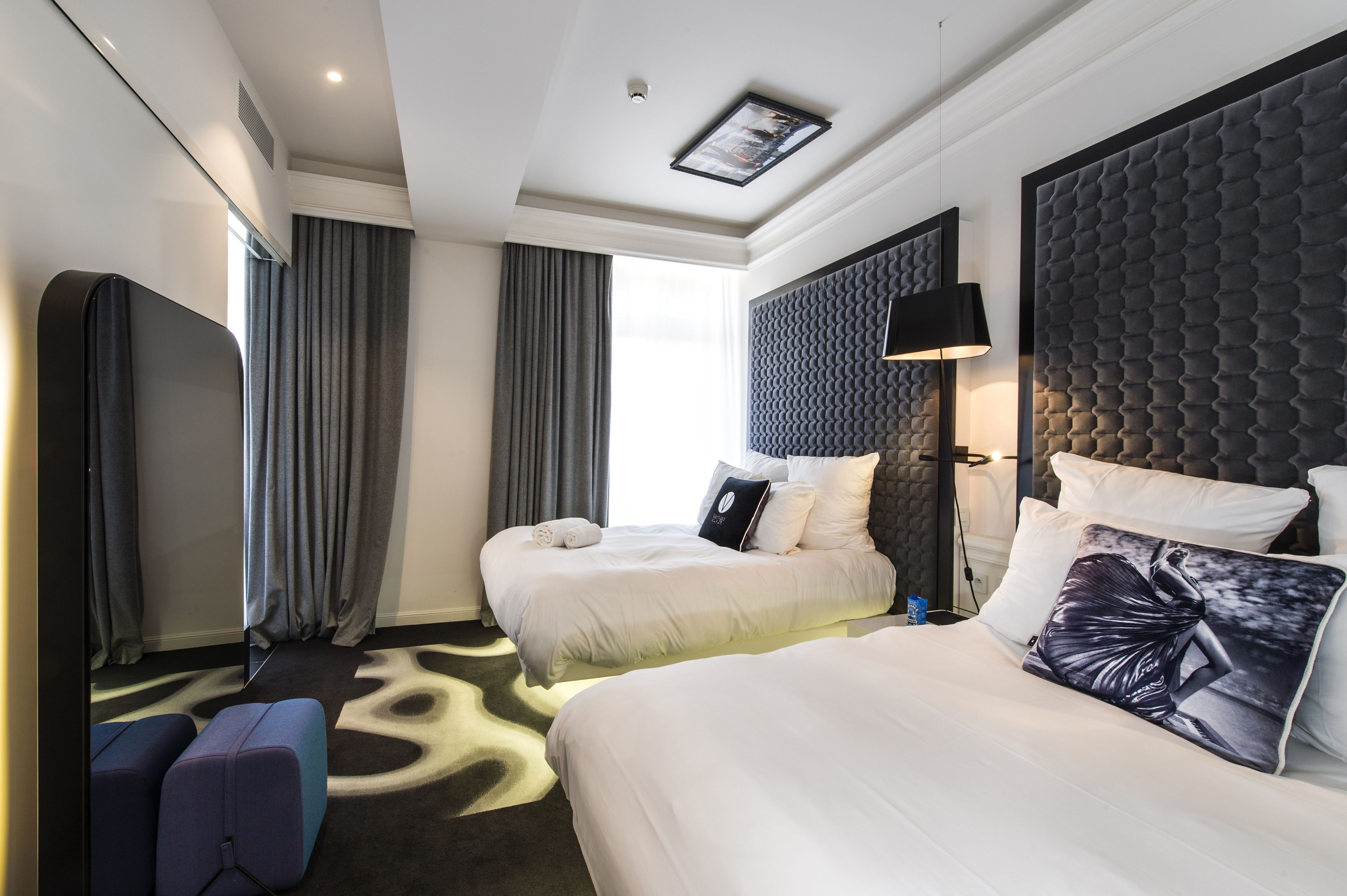 Ett hotellrum med två sängar, ett stort fönster med gardiner, en modern sänggavel och en liten sittgrupp.