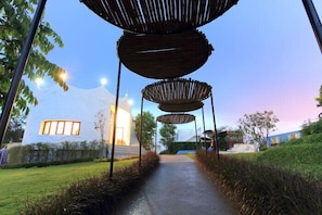 Uma trilha leva a um edifício com uma grande janela e uma estrutura com três elementos de madeira circulares.