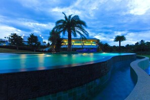 A swimming pool with a curved edge, a palm tree, and a building with illuminated windows in the background. - Gorilla Hills Hua Hin Hotel (Hua Hin)