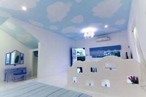 Quarto com cama, escrivaninha e cadeira. Janela com vista para árvores e céu azul.