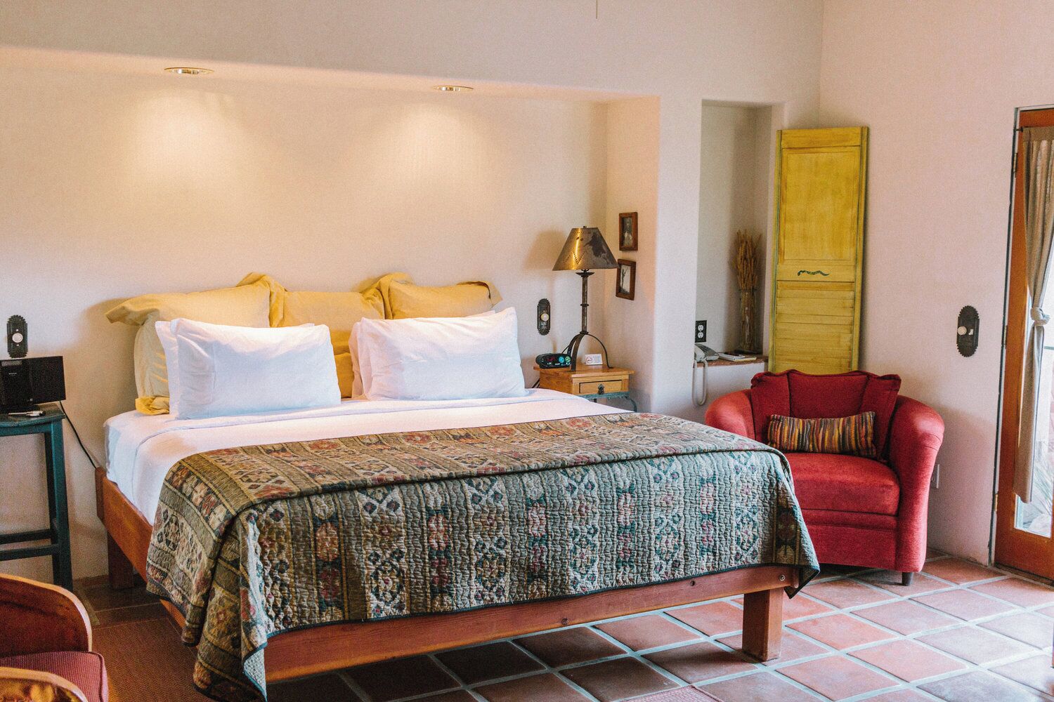 Un dormitorio con cama, mesita de noche, lámpara, silla y espejo.
