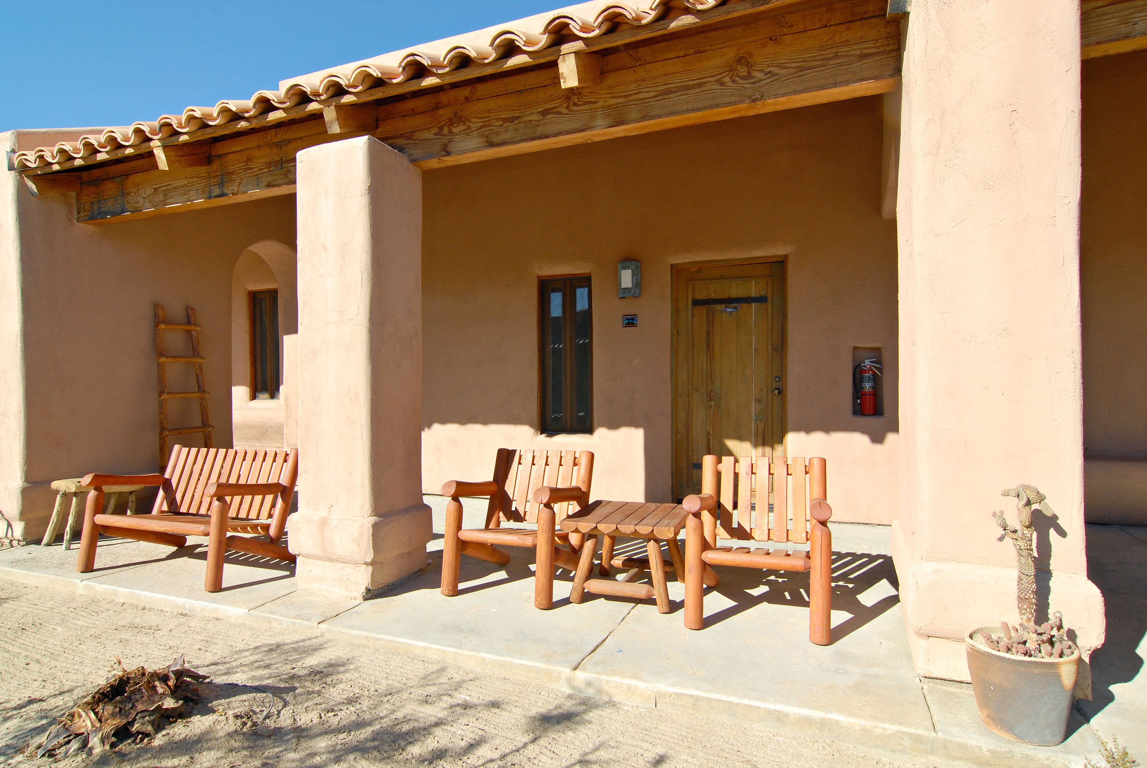 A building with a covered patio area featuring wooden furniture and a potted plant.