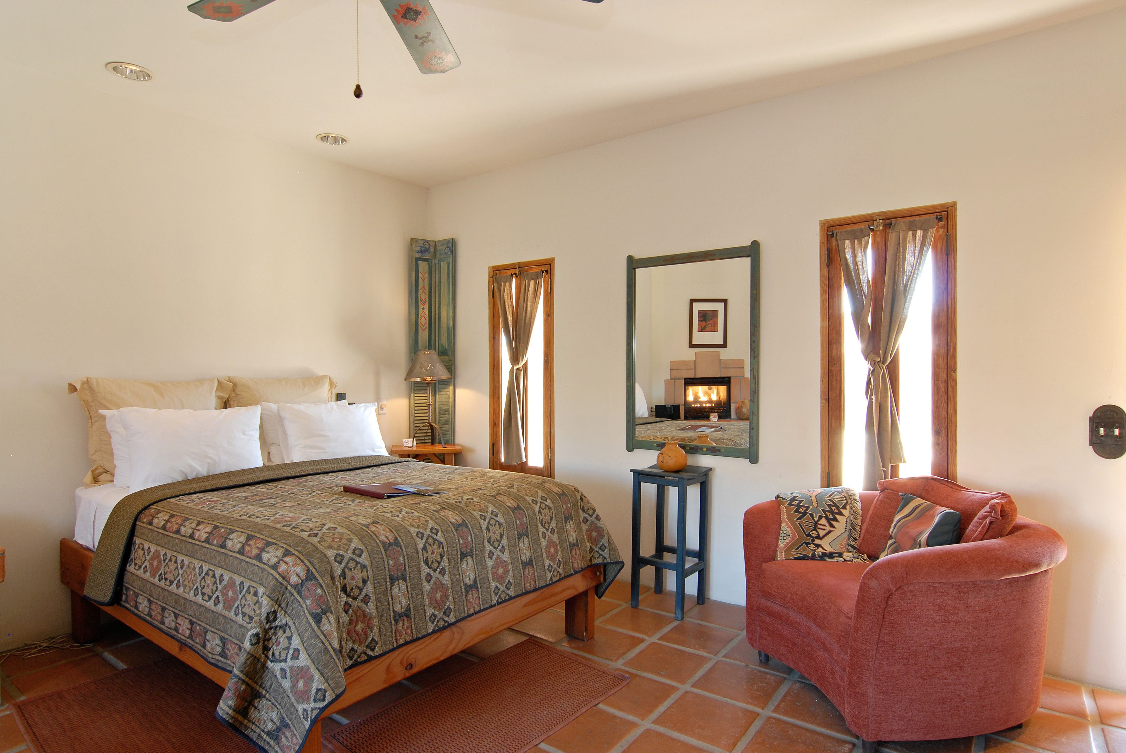 A bedroom with a bed, a chair, a nightstand, a mirror, and a window with curtains.