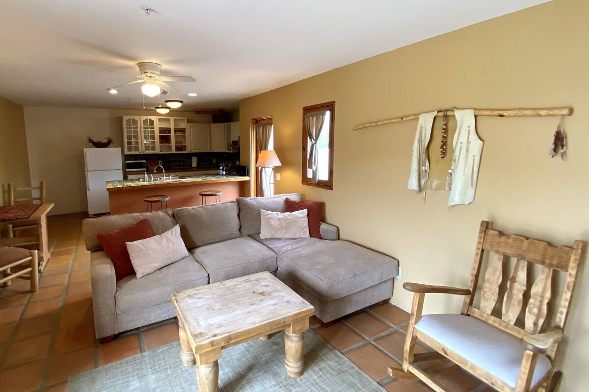 Ein Wohnzimmer mit einer Couch, einem Holztisch, einem Holzstuhl und einer Küche im Hintergrund.