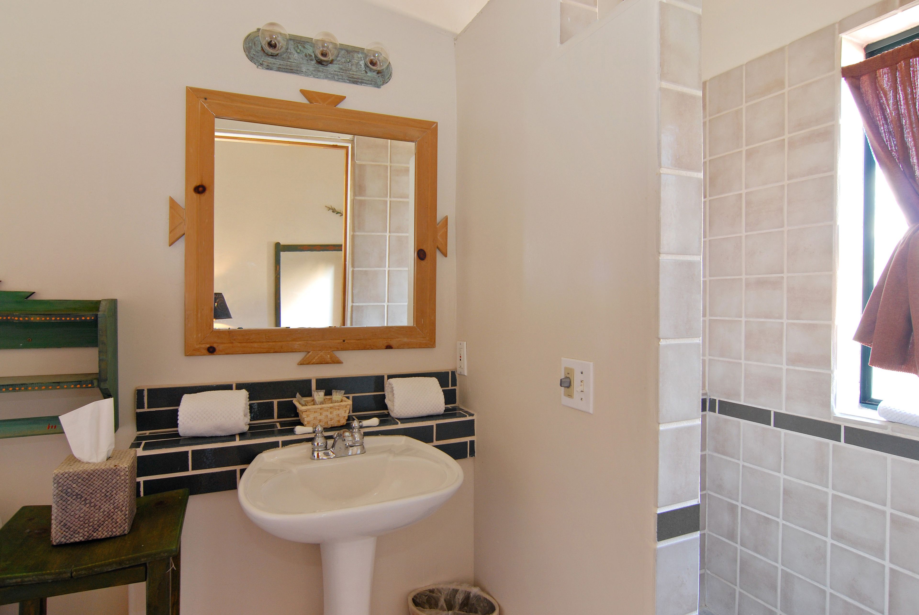 Ein Badezimmer mit einem weißen Waschbecken, einem spiegelnden Wandbild mit Holzrahmen und einem gefliesten Duschbereich.
