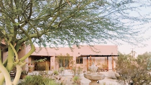 Un bâtiment de style désertique doté d’un patio, d’une fontaine en pierre et de différentes plantes typiques des régions désertiques.