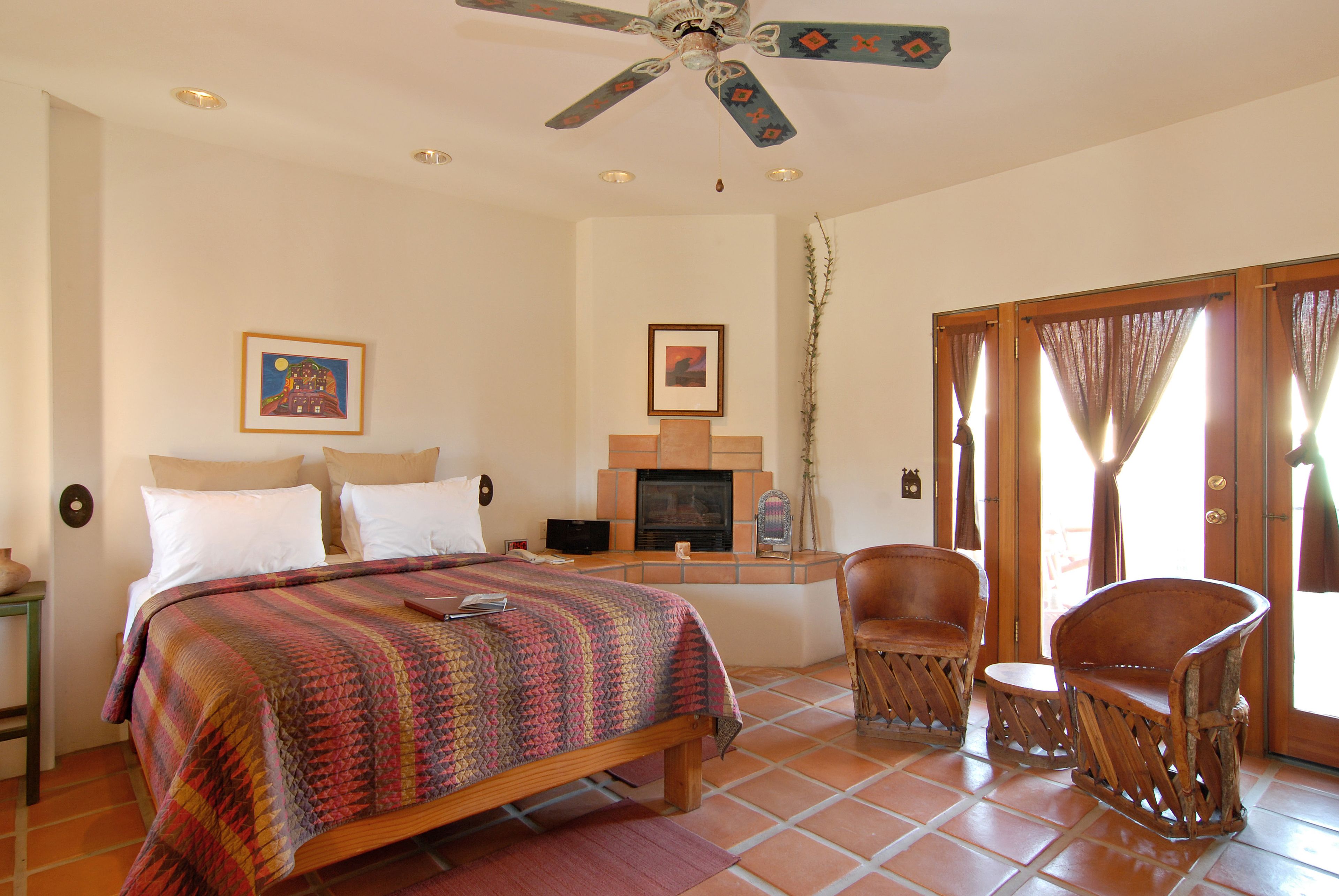 A bedroom with a bed, a television, a fireplace, and two chairs.