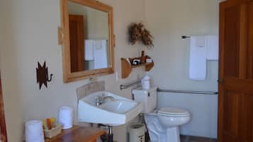 Un baño con tocador de madera, lavamanos blanco, espejo, inodoro y zona de ducha.