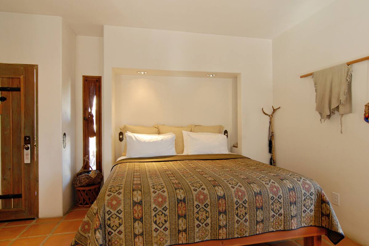 Ein Schlafzimmer mit einem großen Bett, einer Holztür, einem kleinen Fenster und einem an der Wand befestigten Regal.