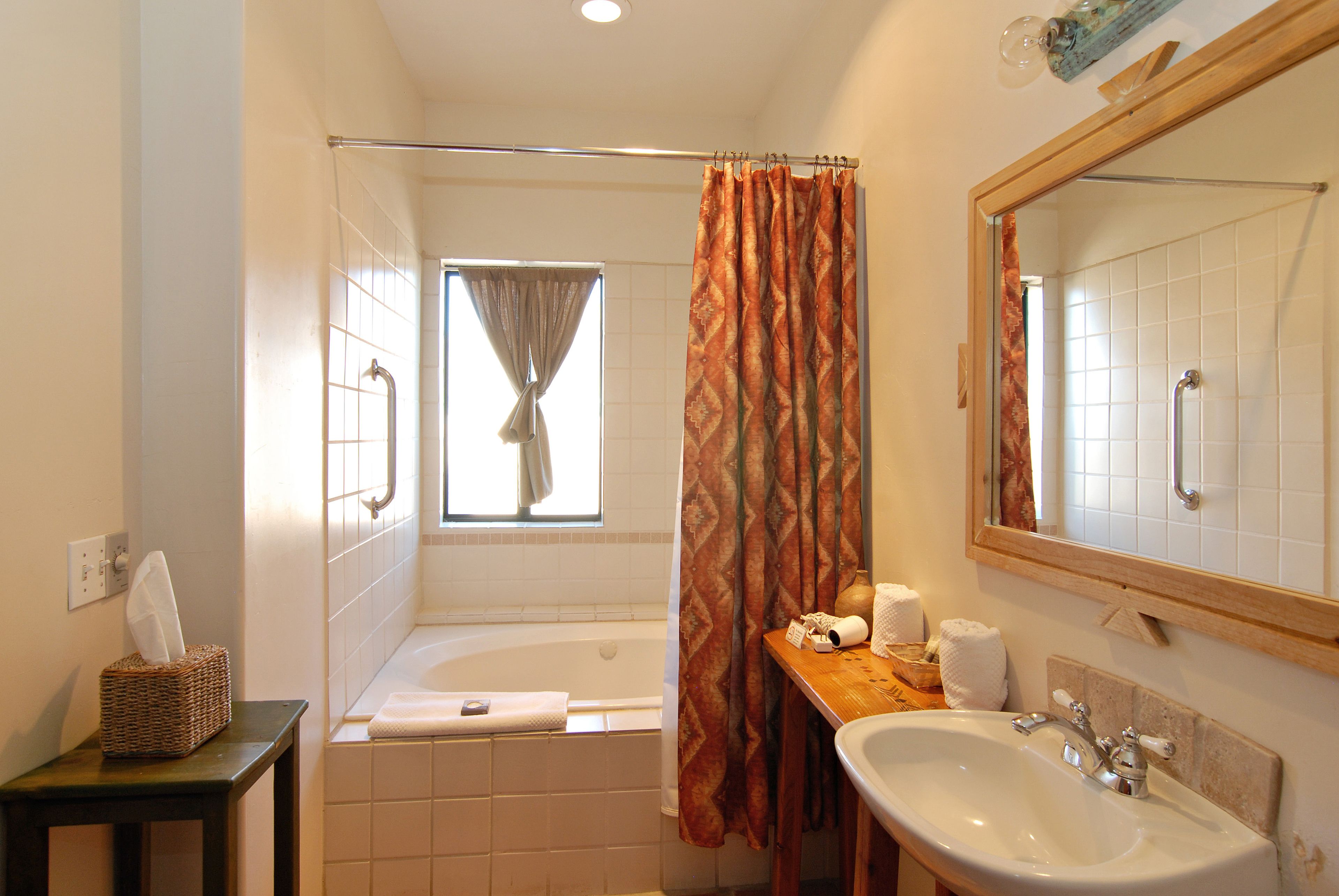 Un baño con bañera, lavamanos, espejo y ventana con cortina.