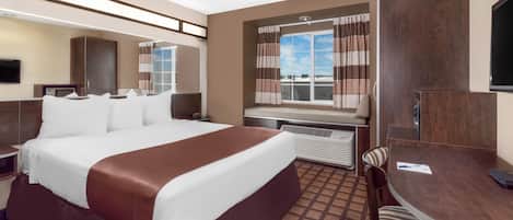 Habitación de hotel con una cama grande, un escritorio, una silla, un televisor y una ventana con cortinas.