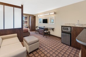 Ein Hotelzimmer mit Sofa, Schreibtisch, Fernseher, Mikrowelle und einer kleinen Küchenzeile.