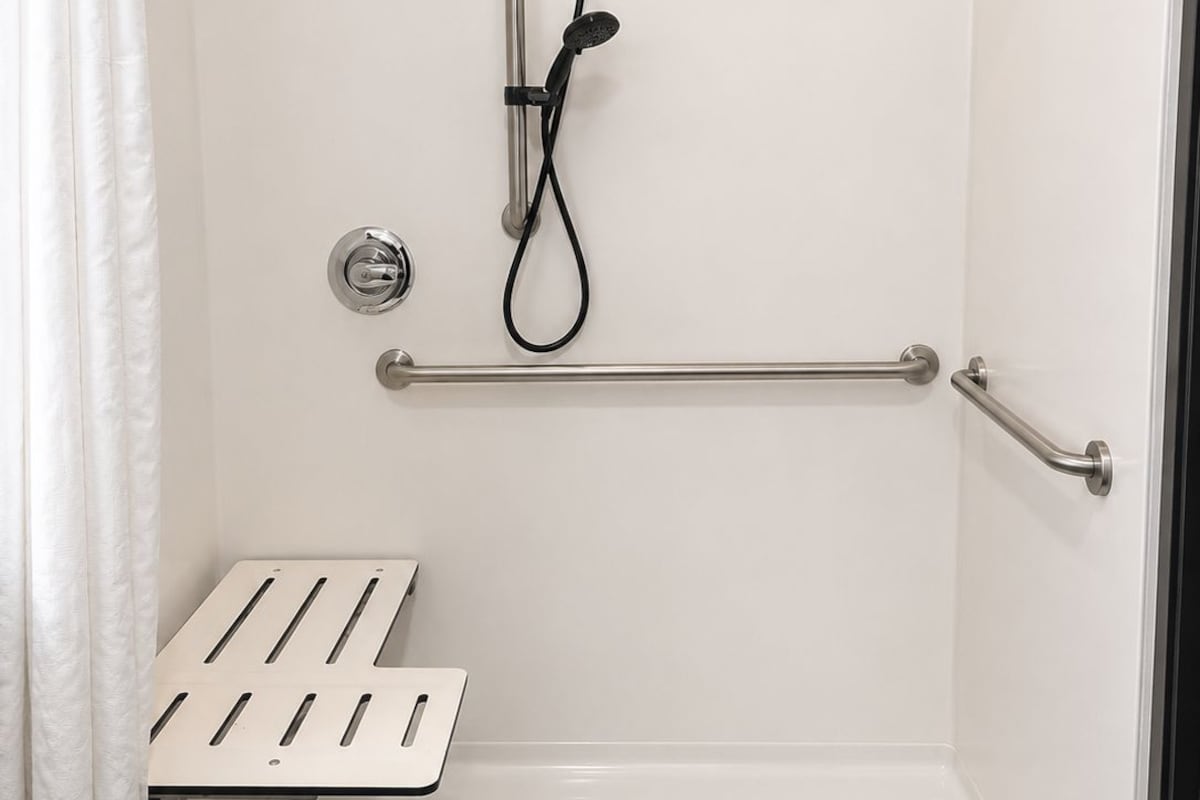 A shower with a grab bar, a showerhead, and a drain.