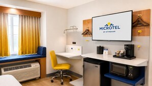 Quarto de hotel com uma cama, uma escrivaninha com computador, micro-ondas e cafeteira.