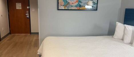 A hotel room with a bed, a door, and a wall-mounted artwork.