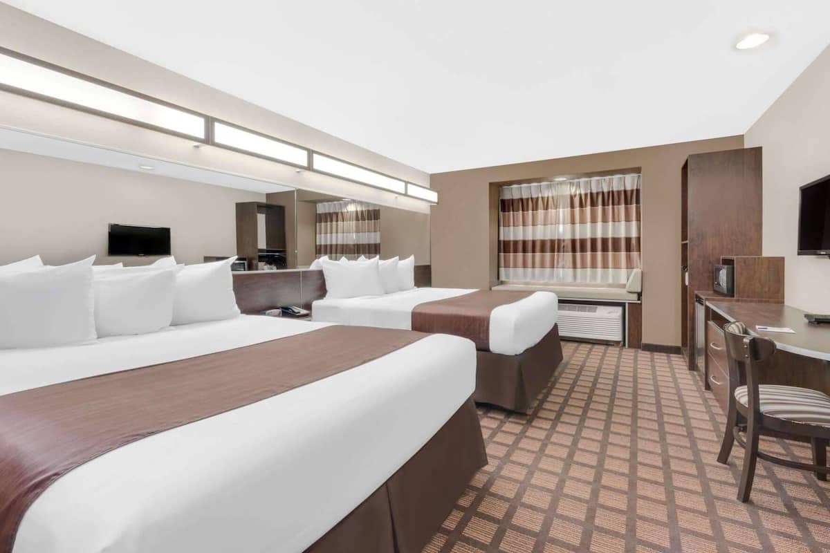 A hotel room with a large bed, a desk, a chair, a television, and a window with curtains.