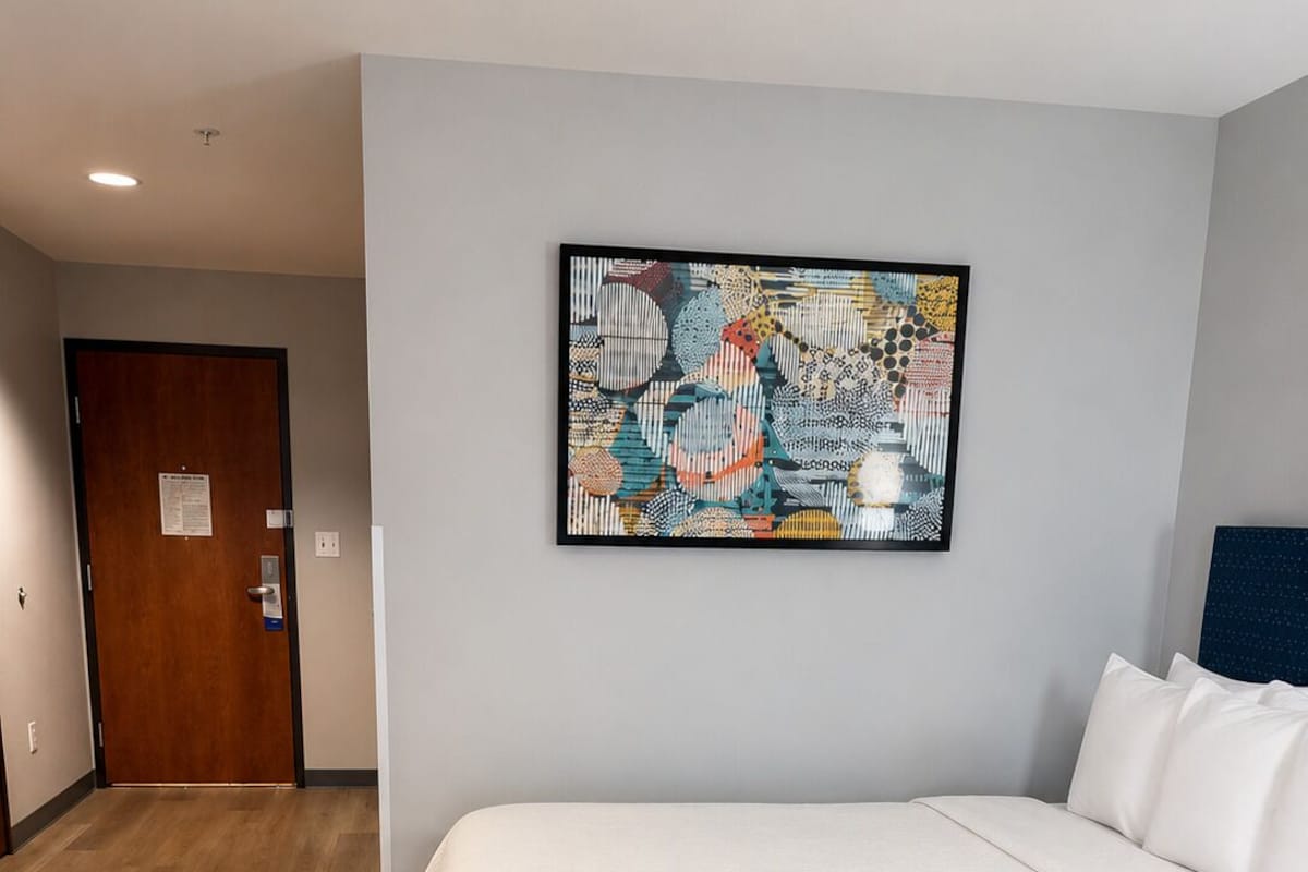 A hotel room with a bed, a door, and a wall-mounted abstract art piece.