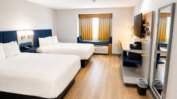 Quarto de hotel com duas camas, uma escrivaninha, televisão e janela com cortinas.