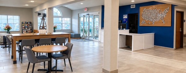 A reception area with a wooden reception desk, a seating area with a round table and chairs, and a wall with a map decoration. - Microtel Inn & Suites By Wyndham Midland (Midland)