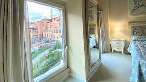 Un dormitorio con una ventana grande, una cama, una mesita de noche y un espejo.