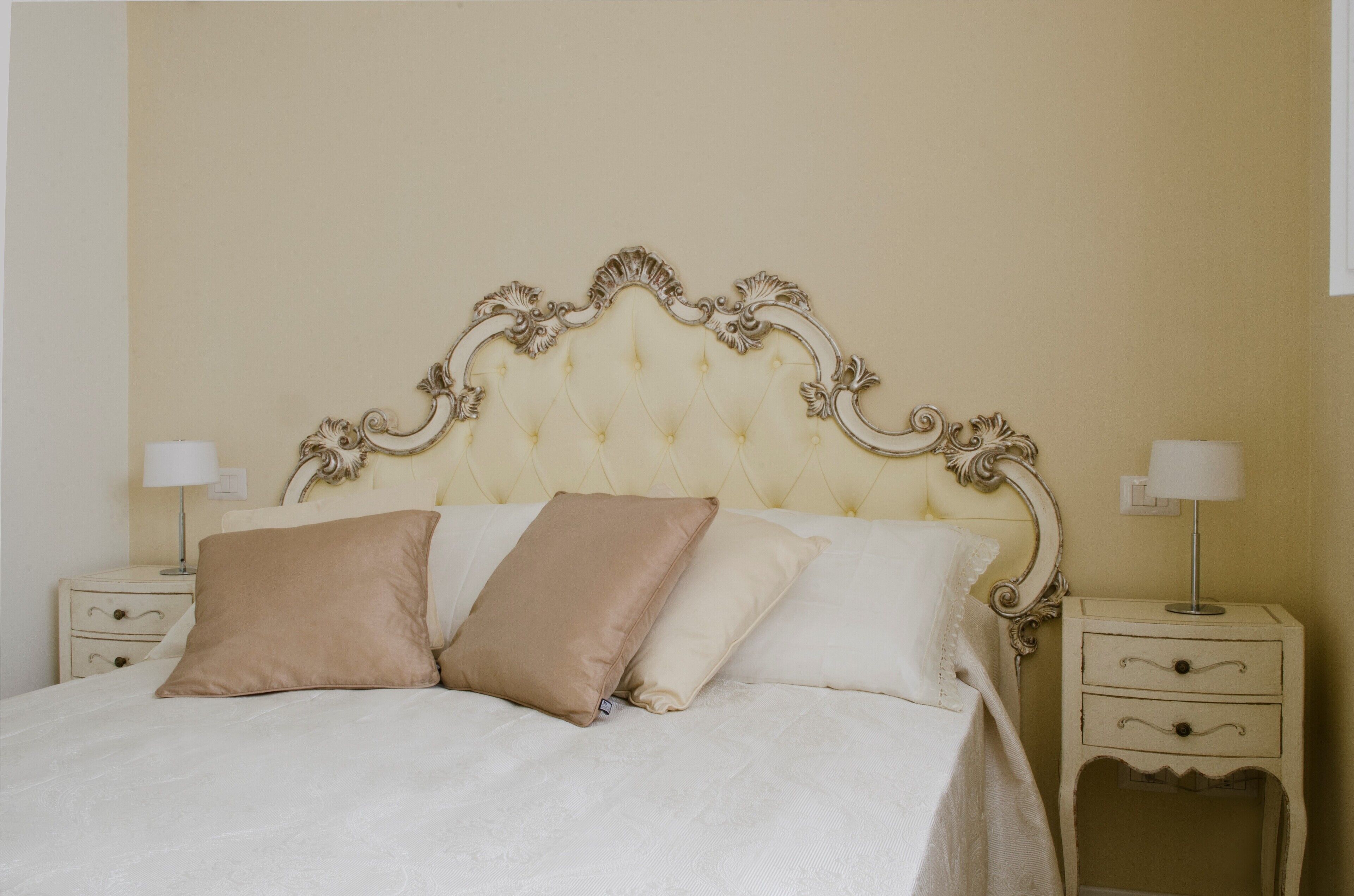 A bed with a tufted headboard, two bedside tables with lamps, and a plain wall.