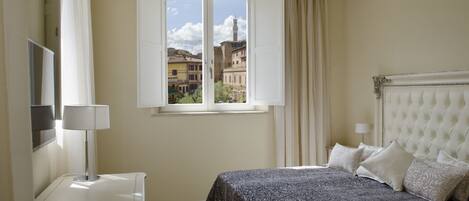 Una habitación de hotel con cama, televisión, ventana con cortinas y vistas a edificios.