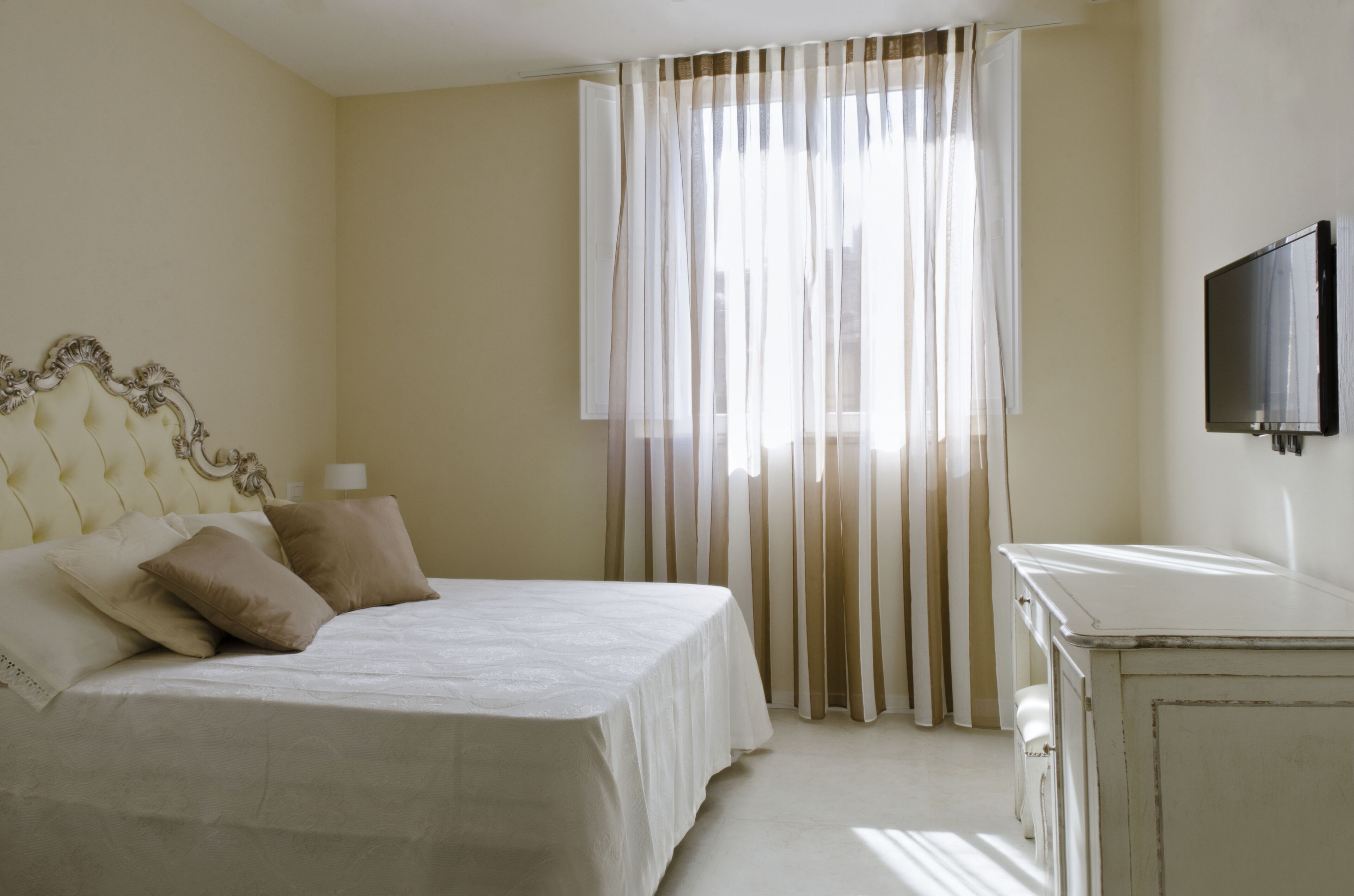 A bedroom with a bed, curtains, a TV, and a dresser.