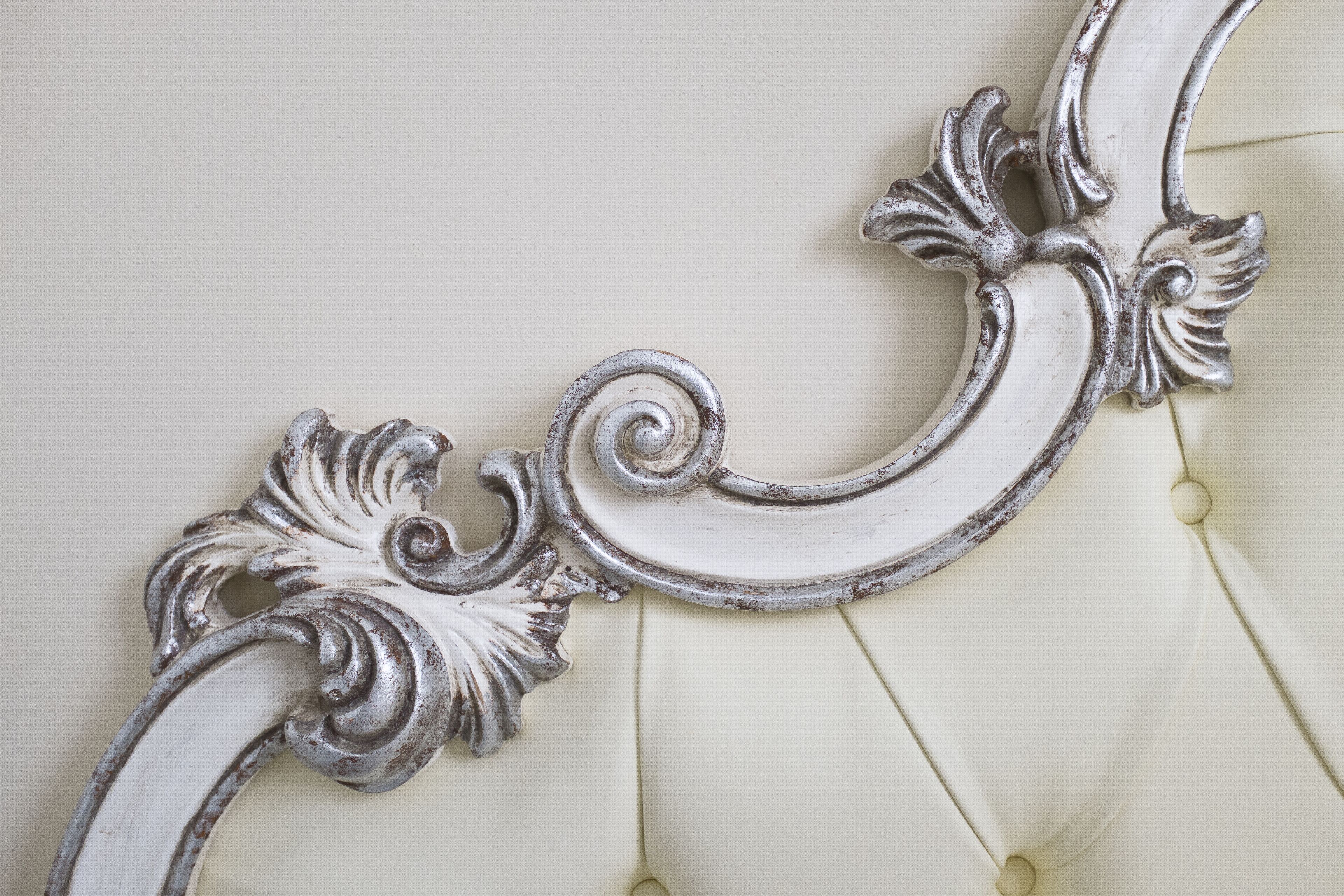 A close-up of a white, ornate, and slightly worn decorative element on a piece of furniture, likely a headboard or armrest.