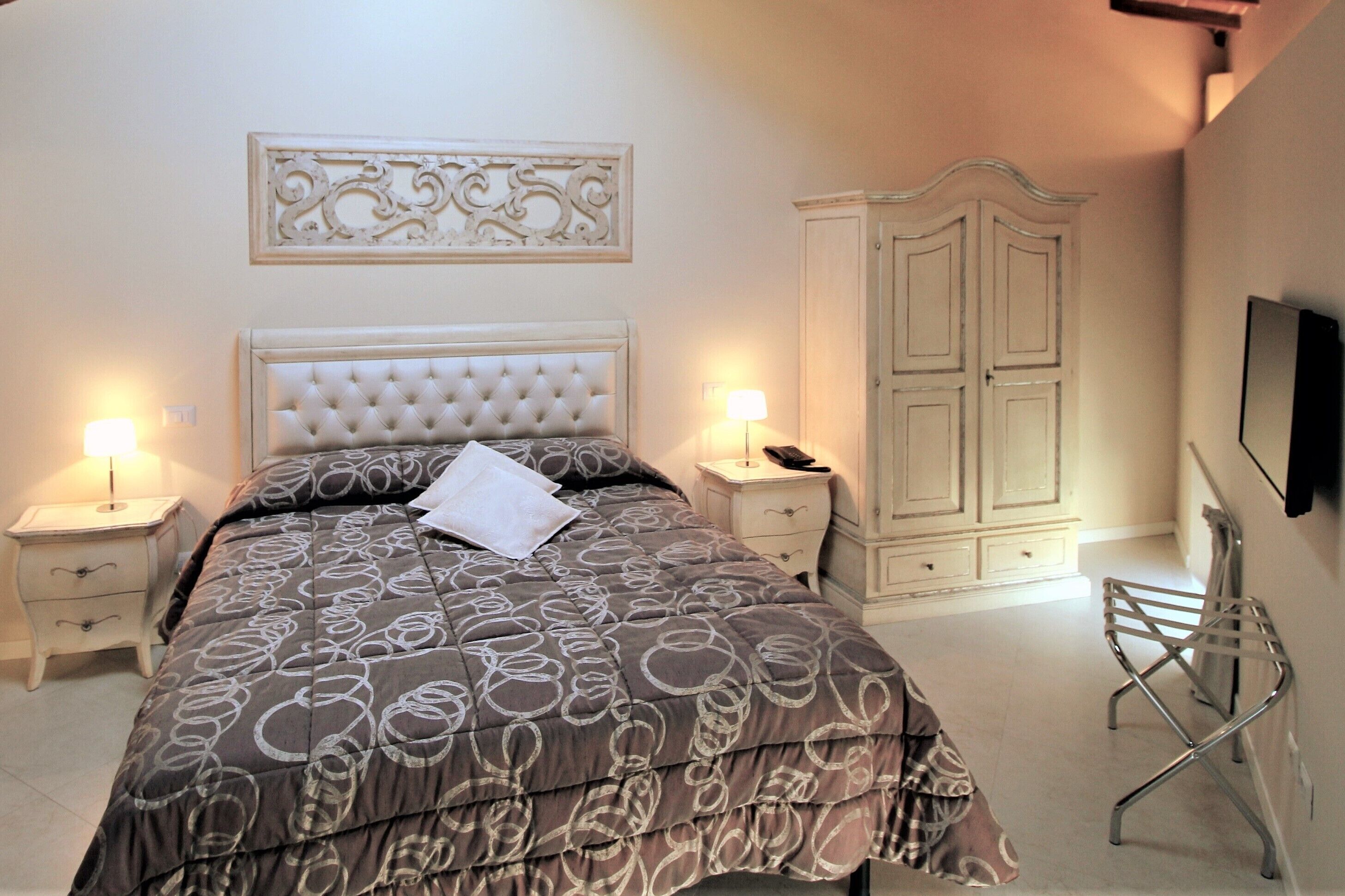 A bedroom with a large bed, two bedside tables with lamps, a wardrobe, and a TV mounted on the wall.