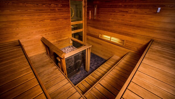 A sauna with wooden walls and a stone floor, featuring a small window and a wooden bench. - Park Hotel Turku (Turku)