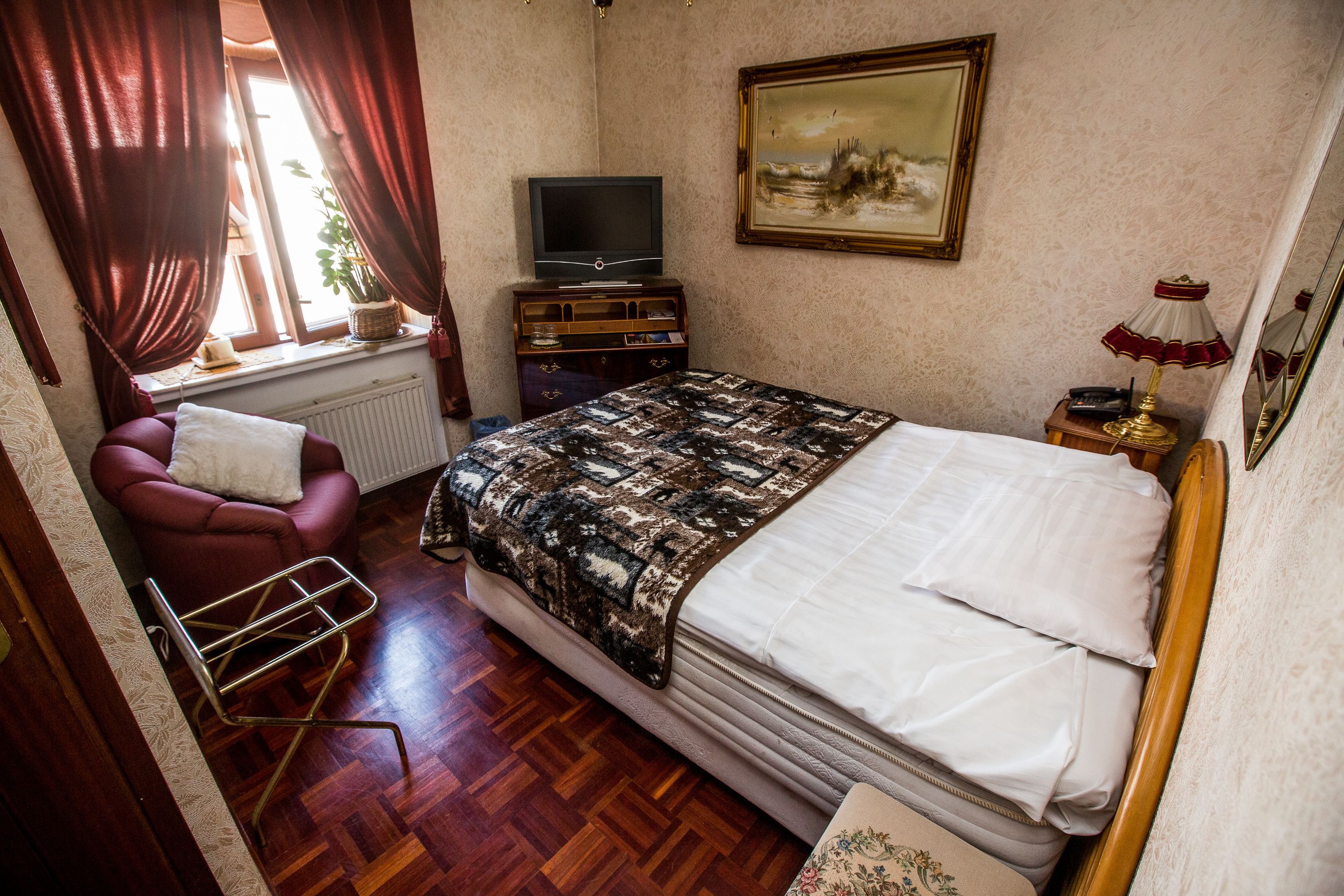 A bedroom with a bed, a chair, a television, a dresser, and a painting on the wall.