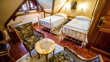 A bedroom with two beds, a wooden floor, a small round table, and floral-patterned chairs.