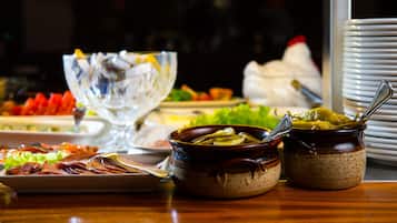 Een buffettafel met diverse gerechten, waaronder een schaal augurken, een bord met vleesschijfjes en een glazen schaal met een lepel.
