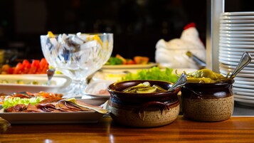 Una mesa de buffet con diversos platos, incluyendo un bol de pepinillos, un plato de carnes en rodajas y un bol de vidrio con una cuchara.