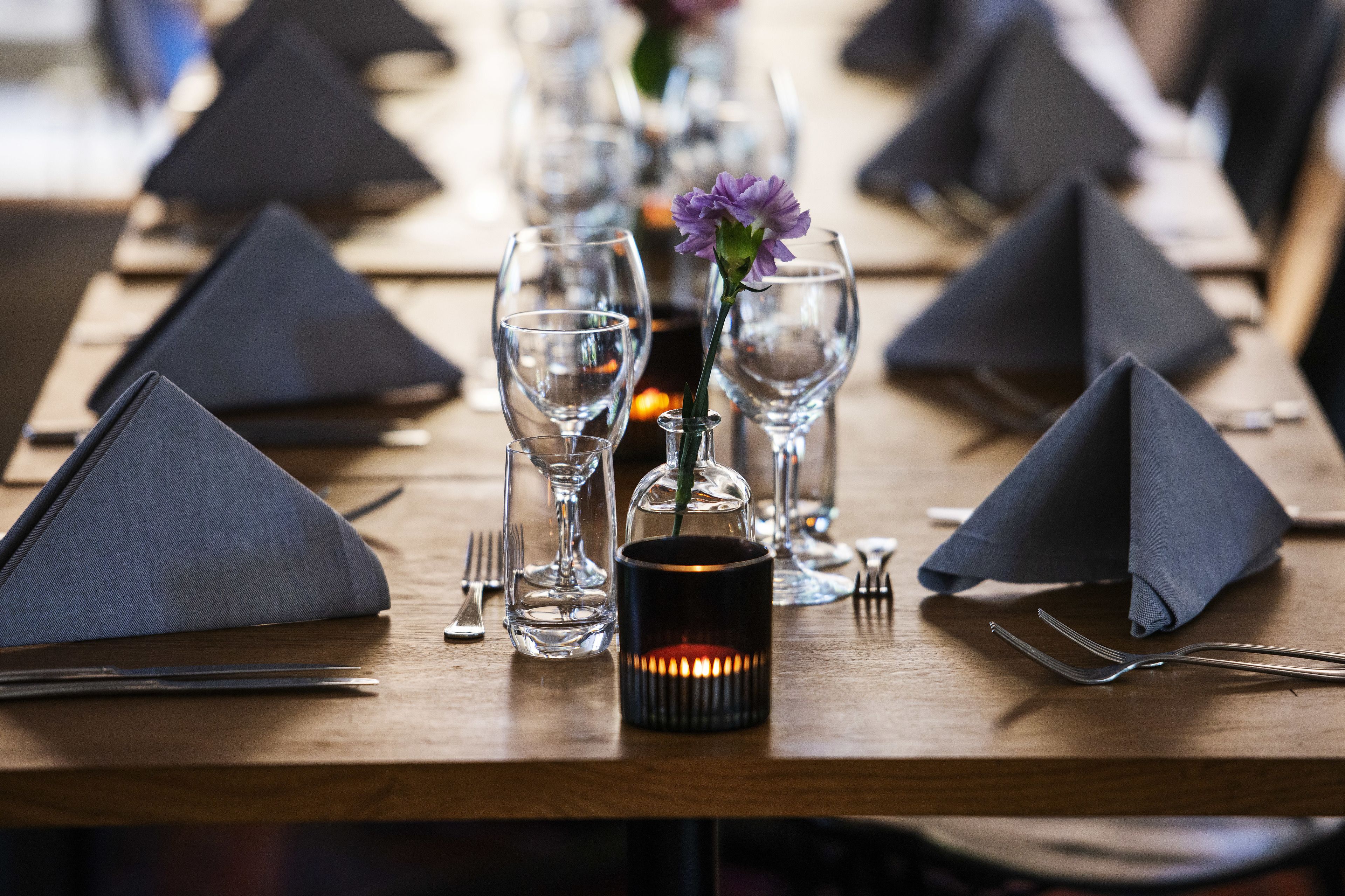 Una mesa de comedor dispuesta con servilletas oscuras, copas de vino transparentes y una vela.