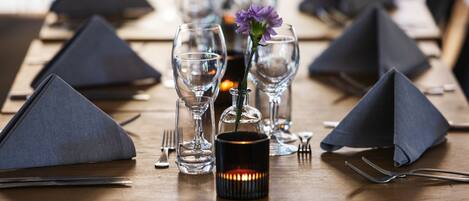 Una mesa de comedor dispuesta con servilletas oscuras, copas de vino transparentes y una vela.
