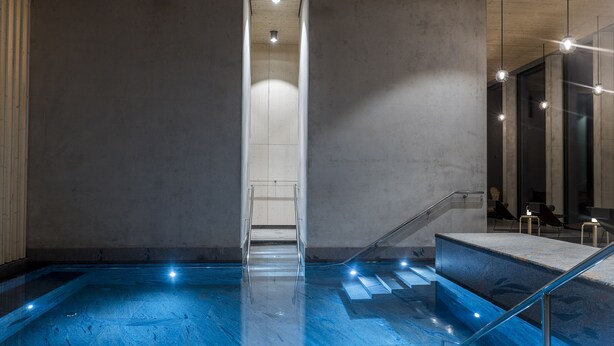 A modern indoor pool area with clear glass railings, a central staircase, and ambient lighting.