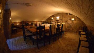 A dining area with a long table and chairs, stone walls, and a brick floor.