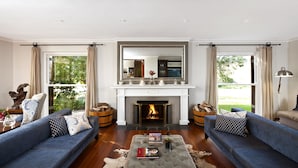 A spacious living room with a fireplace, two sofas, a coffee table, and large windows with curtains. - The Lodge L'Avenir (Stellenbosch)