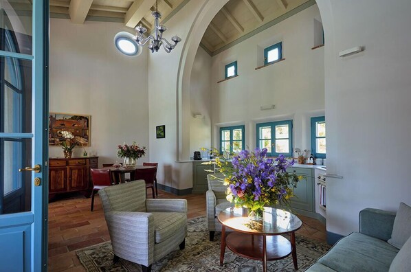 A spacious living room with a high ceiling, a dining area, and a kitchen with blue accents. - Borgo Pignano Volterra Tuscany (Volterra)