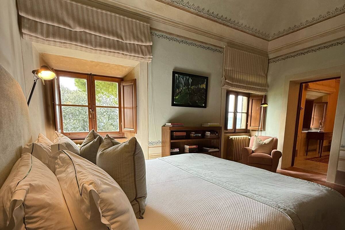 Una cama grande con múltiples almohadas, un televisor montado en la pared y una estantería.