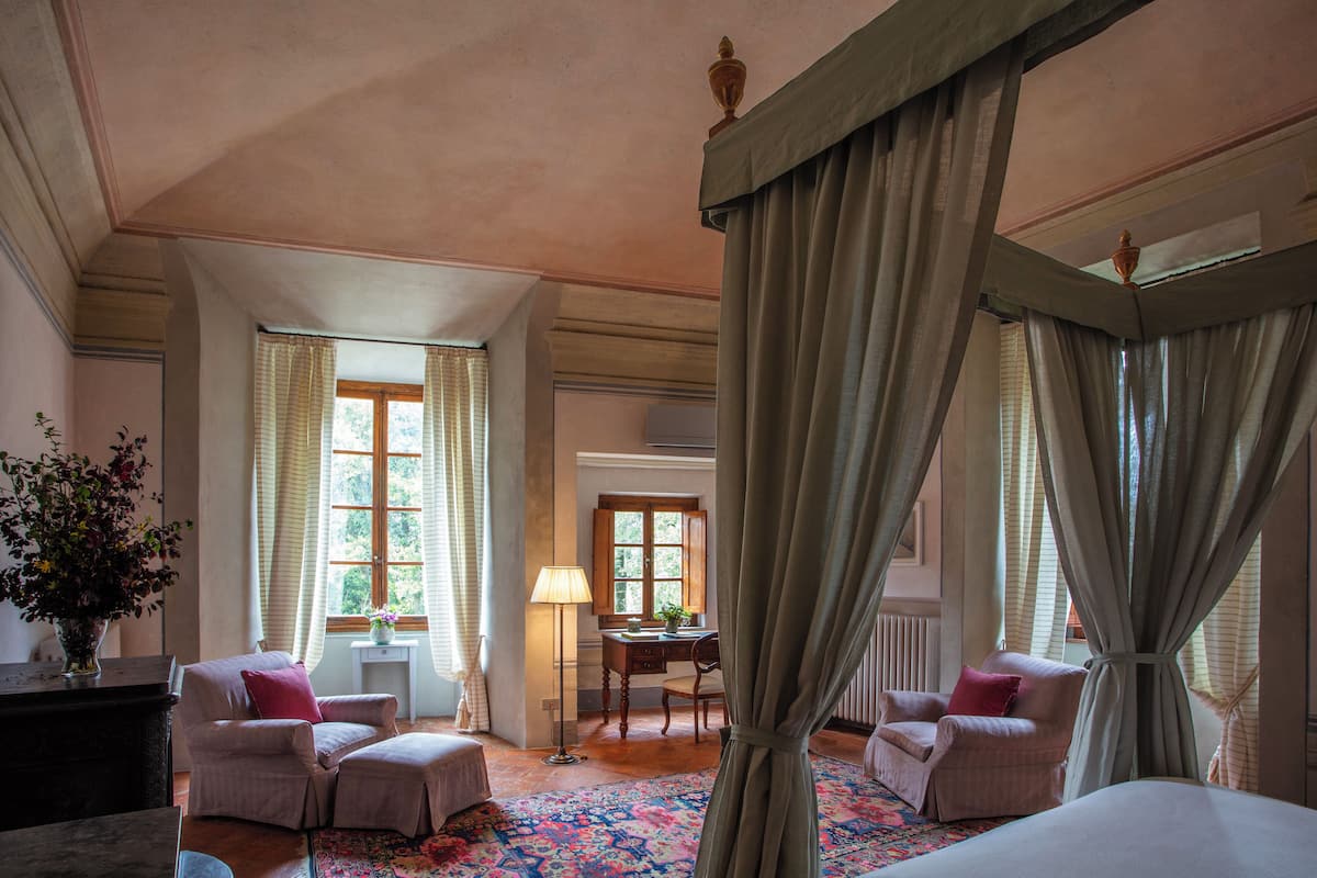 Una habitación con cama a dosel, dos sillones, un escritorio y una ventana con cortinas.